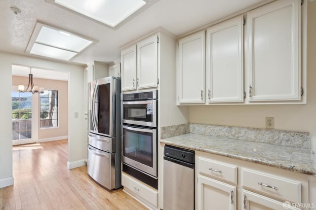 kitchen featuring stainless steel appliances, white cabinets, light stone counters, and light hardwood / wood-style flooring