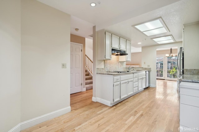 kitchen featuring sink, tasteful backsplash, black electric cooktop, dishwasher, and light hardwood / wood-style floors