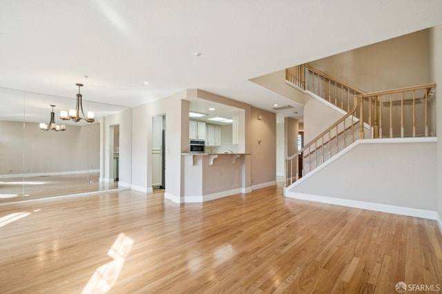 unfurnished living room featuring a notable chandelier and light hardwood / wood-style floors