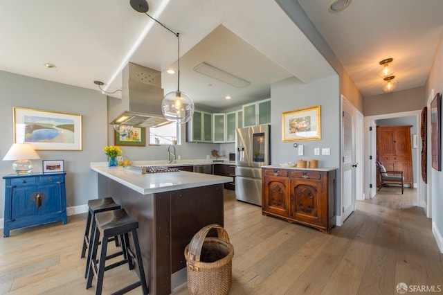 kitchen with light wood-style flooring, a kitchen breakfast bar, range hood, stainless steel appliances, and light countertops