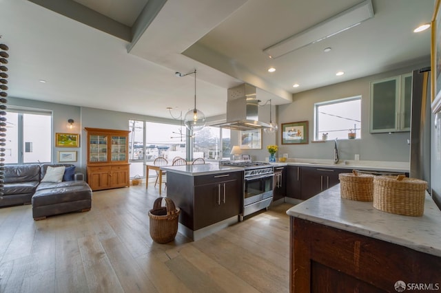 kitchen featuring high end range, a peninsula, island exhaust hood, light wood-style floors, and a sink