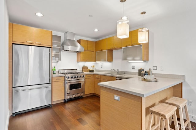 kitchen featuring kitchen peninsula, hanging light fixtures, stainless steel appliances, wall chimney range hood, and a breakfast bar