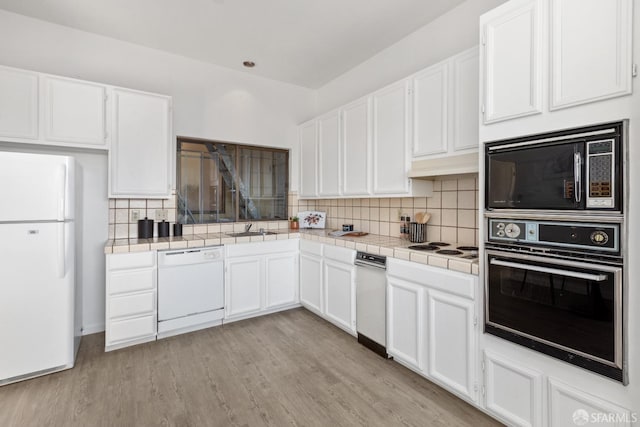 kitchen featuring white appliances, white cabinetry, backsplash, tile counters, and light wood-type flooring