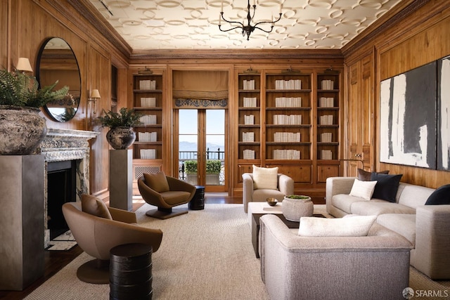 sitting room featuring french doors, a notable chandelier, wooden walls, and ornamental molding