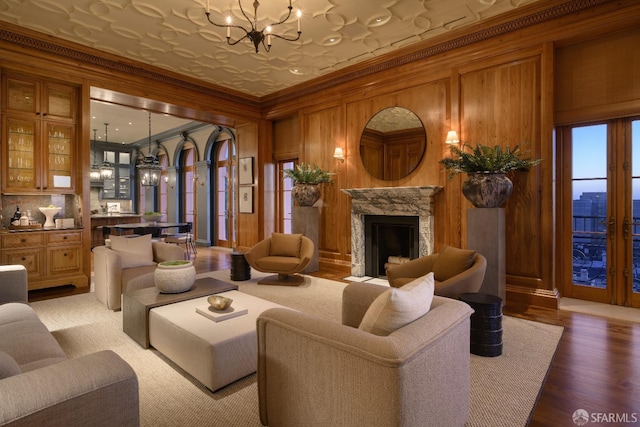 living room featuring hardwood / wood-style flooring, wood walls, a notable chandelier, and a high end fireplace