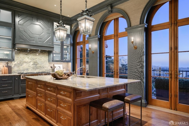 kitchen featuring an island with sink, french doors, decorative light fixtures, ornamental molding, and sink