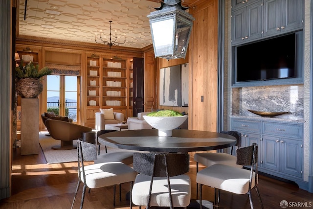 dining room featuring dark hardwood / wood-style flooring, a chandelier, wood walls, crown molding, and built in features