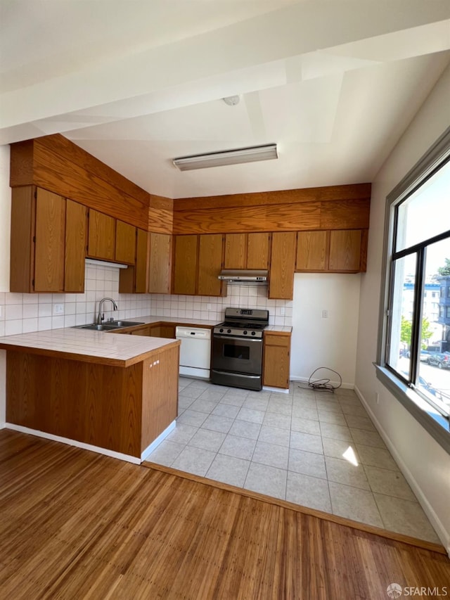 kitchen featuring backsplash, kitchen peninsula, dishwasher, light wood-type flooring, and stainless steel range