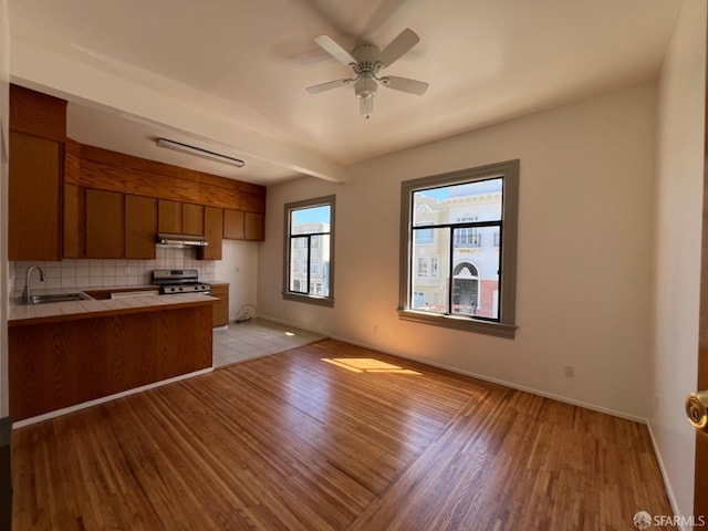 kitchen with tile countertops, light wood-type flooring, stainless steel range oven, ceiling fan, and sink