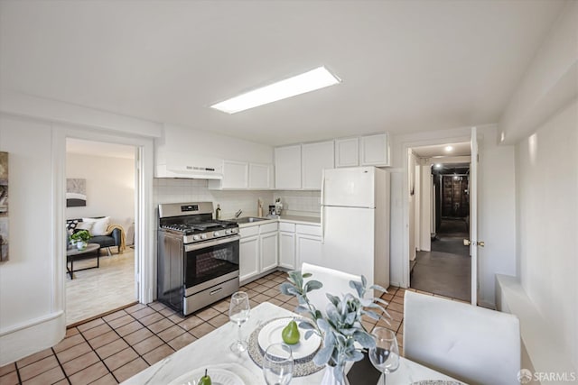 kitchen with tasteful backsplash, light tile patterned floors, white cabinets, stainless steel range with gas stovetop, and white refrigerator