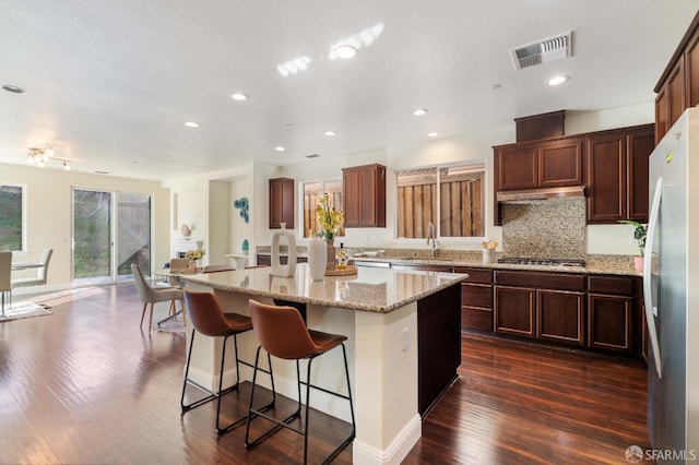 kitchen with sink, a center island with sink, appliances with stainless steel finishes, dark hardwood / wood-style floors, and light stone countertops