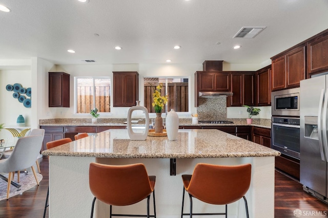 kitchen featuring light stone counters, appliances with stainless steel finishes, dark wood-type flooring, and a kitchen island