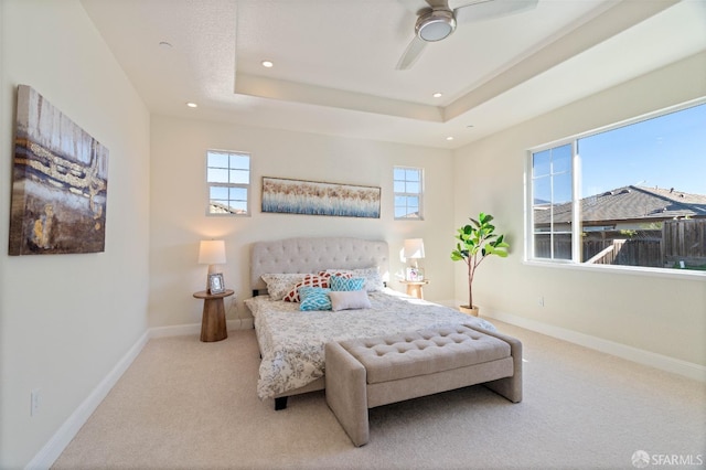 carpeted bedroom featuring a raised ceiling, ceiling fan, and multiple windows