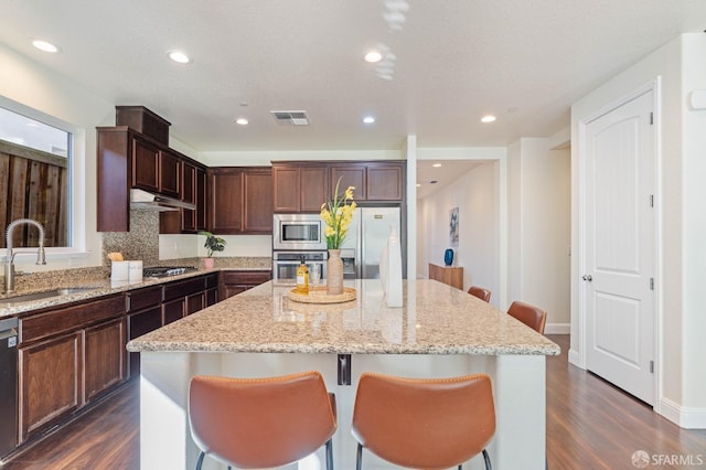 kitchen with dark wood-type flooring, sink, light stone counters, a kitchen island, and stainless steel appliances