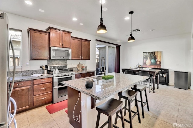 kitchen with sink, a breakfast bar area, a kitchen island with sink, light stone counters, and stainless steel appliances