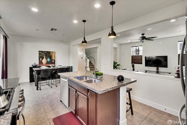 kitchen with sink, appliances with stainless steel finishes, a center island with sink, light tile patterned flooring, and decorative light fixtures