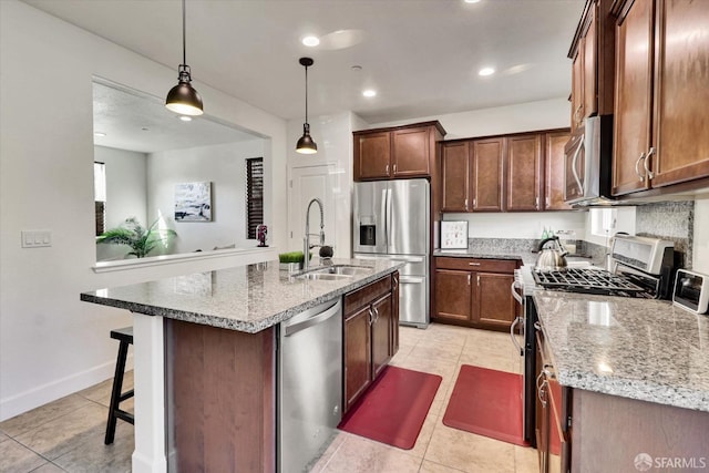 kitchen with sink, light stone counters, hanging light fixtures, a center island with sink, and appliances with stainless steel finishes