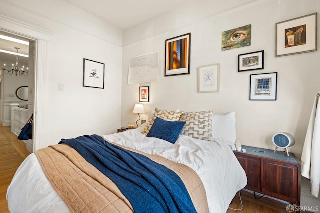 bedroom with ensuite bathroom, a notable chandelier, and hardwood / wood-style flooring