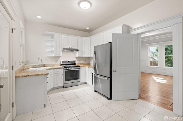 kitchen with light stone countertops, appliances with stainless steel finishes, sink, light tile patterned floors, and white cabinets