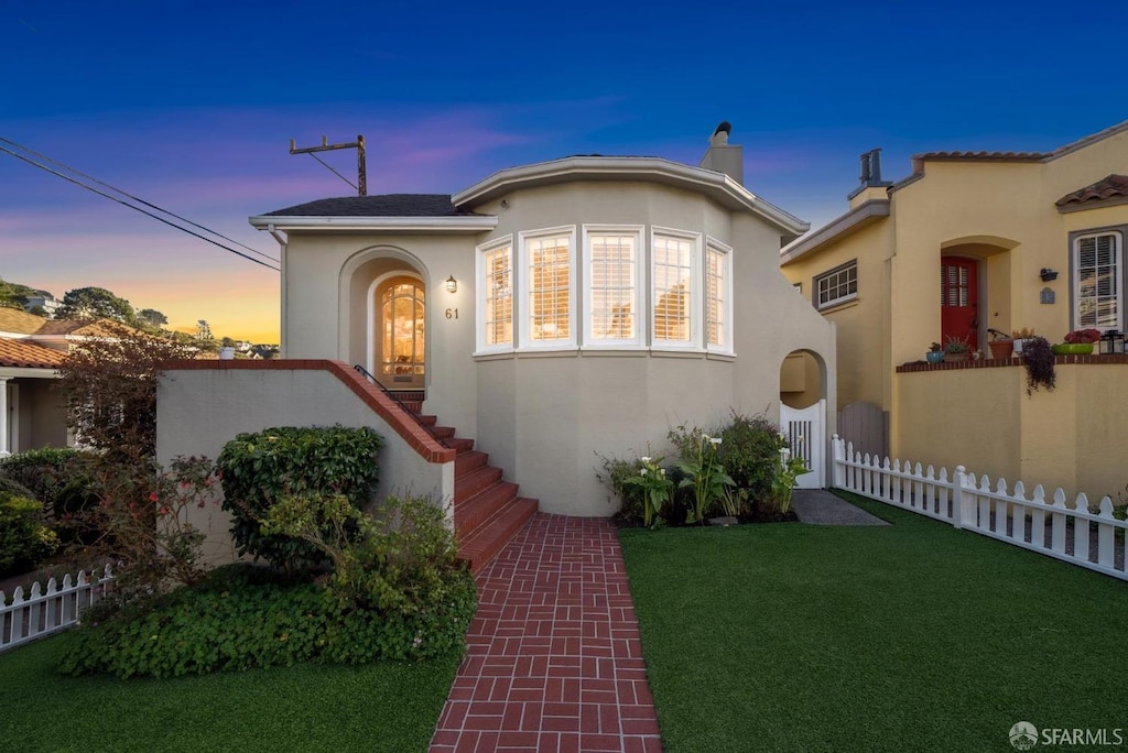 view of front facade featuring a front yard, a chimney, fence, and stucco siding