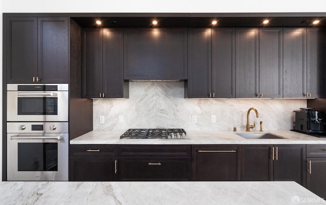 kitchen with light stone counters, tasteful backsplash, appliances with stainless steel finishes, a sink, and dark brown cabinetry