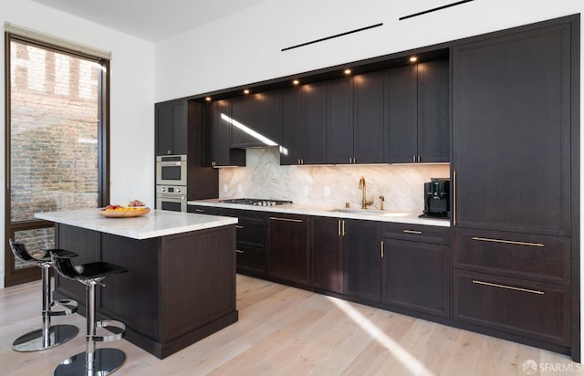 kitchen with a kitchen island, appliances with stainless steel finishes, a breakfast bar area, light wood-type flooring, and a sink