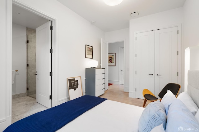 bedroom with ensuite bathroom, visible vents, light wood-style floors, baseboards, and a closet