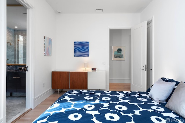 bedroom with light wood finished floors, ensuite bath, and baseboards