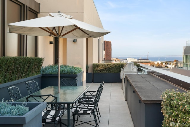 balcony featuring a water view, an outdoor kitchen, a patio, and outdoor dining space