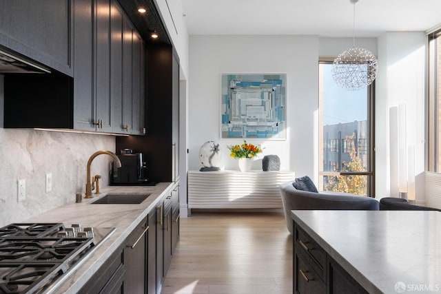 kitchen featuring light wood-style flooring, decorative light fixtures, light countertops, stainless steel gas stovetop, and a sink