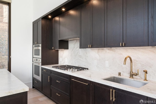 kitchen featuring appliances with stainless steel finishes, a sink, light wood finished floors, and tasteful backsplash