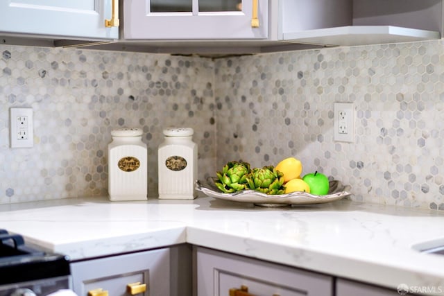 kitchen with wall chimney range hood, tasteful backsplash, and light stone counters