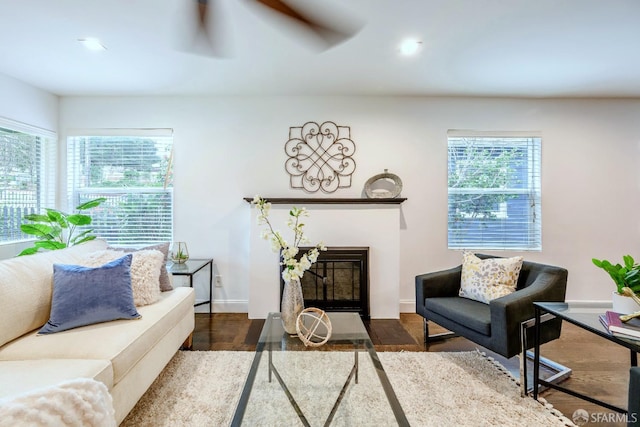 living room featuring a fireplace with flush hearth, baseboards, ceiling fan, and wood finished floors