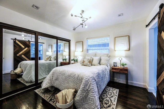 bedroom featuring wood finished floors, visible vents, baseboards, and a barn door