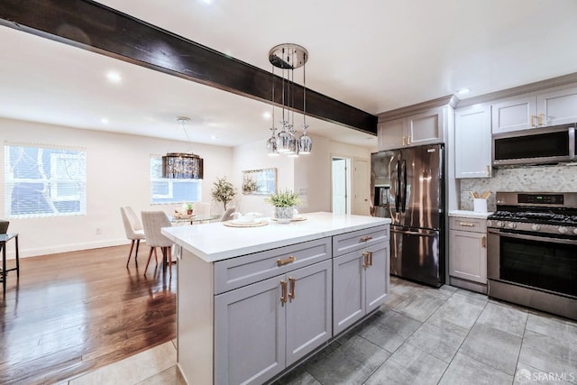 kitchen featuring gray cabinetry, stainless steel appliances, light countertops, backsplash, and beamed ceiling