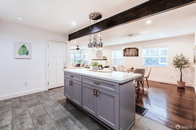 kitchen featuring plenty of natural light, beamed ceiling, a center island, gray cabinets, and light countertops