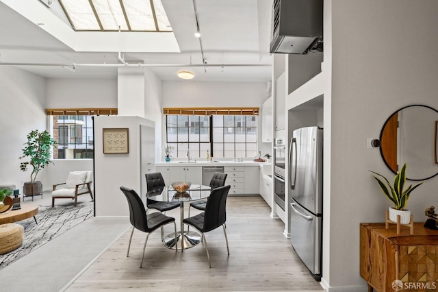 dining room featuring light hardwood / wood-style flooring, a wealth of natural light, track lighting, and a skylight