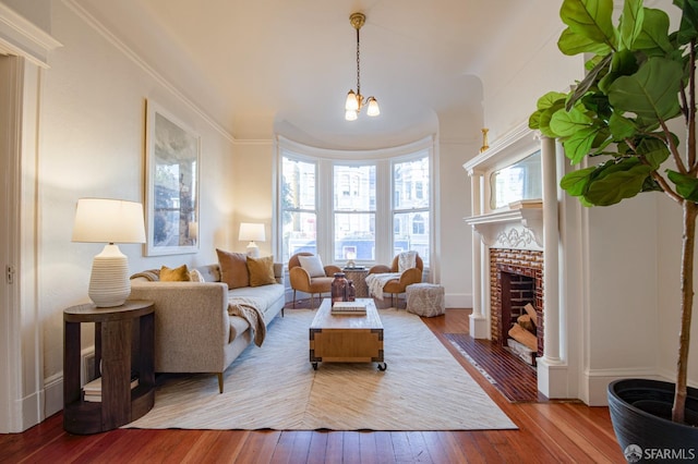 living room with wood-type flooring, crown molding, a chandelier, and a fireplace