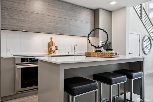 1605 Riviera Ave Unit 608, Walnut Creek, CA 94596 - kitchen featuring oven, a kitchen bar, modern cabinets, gray cabinetry, and light stone countertops
