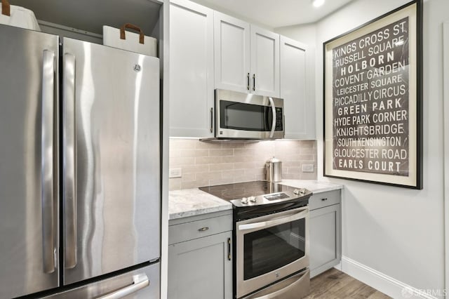 kitchen featuring stainless steel appliances, wood finished floors, baseboards, light stone countertops, and tasteful backsplash