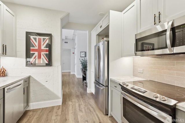 kitchen with light wood-type flooring, tasteful backsplash, appliances with stainless steel finishes, and light stone counters