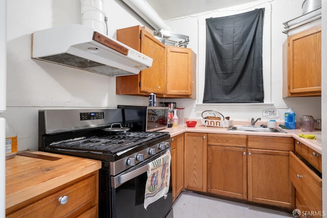 kitchen with butcher block counters, brown cabinetry, a sink, stainless steel gas range, and under cabinet range hood