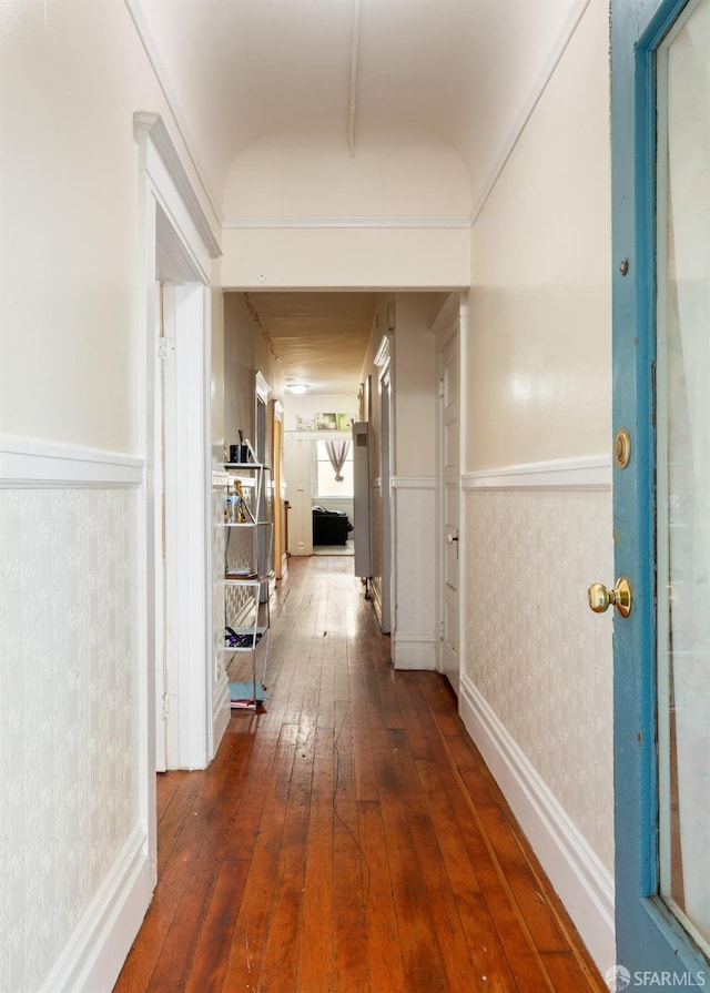 hallway with lofted ceiling, wallpapered walls, dark wood-style flooring, and wainscoting