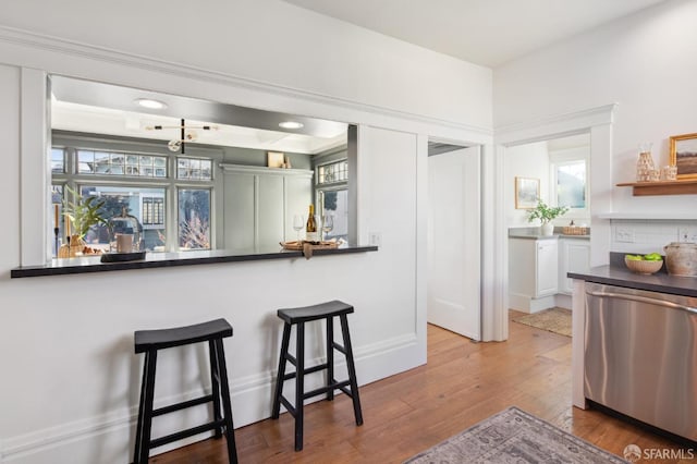 kitchen with light hardwood / wood-style flooring, stainless steel dishwasher, white cabinets, and a kitchen bar