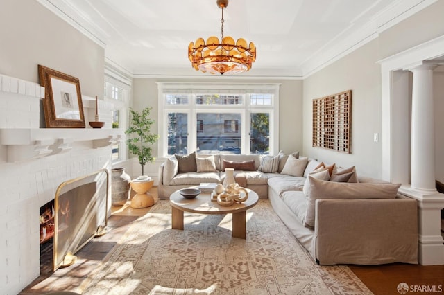 living room with a chandelier, crown molding, a fireplace, and decorative columns