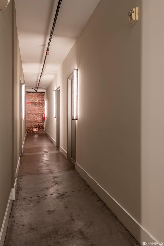 corridor with track lighting, brick wall, concrete flooring, and baseboards