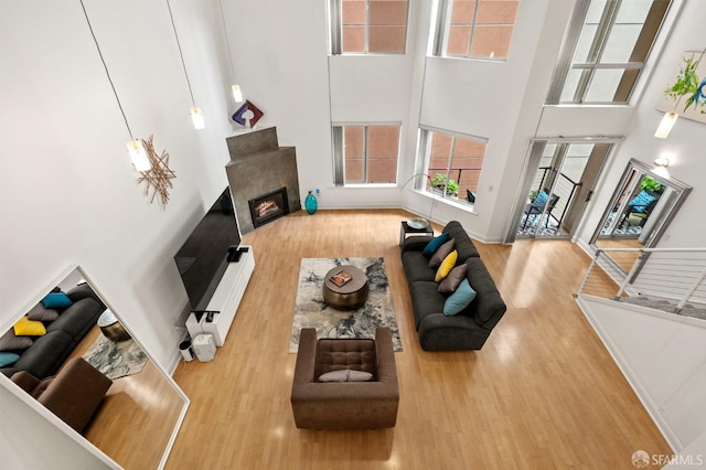 living area with a glass covered fireplace, a towering ceiling, and wood finished floors