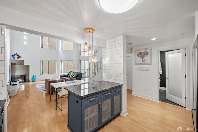 kitchen with light wood-style flooring, decorative light fixtures, open floor plan, a lit fireplace, and blue cabinets