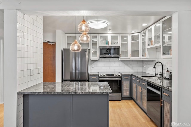 kitchen featuring appliances with stainless steel finishes, a sink, dark stone countertops, a peninsula, and tasteful backsplash