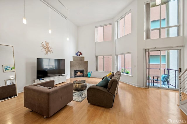 living area featuring baseboards, a high ceiling, wood finished floors, and a lit fireplace